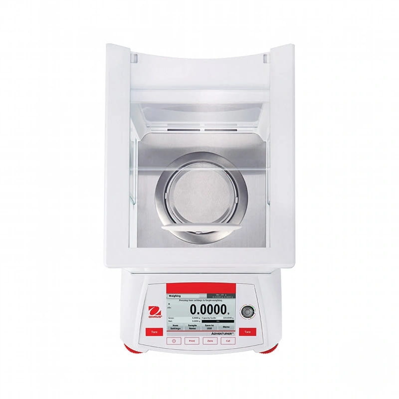 White analytical balance with a digital display showing ’0.0000’’ and red branding, featuring a transparent weighing chamber with a circular metal tray inside