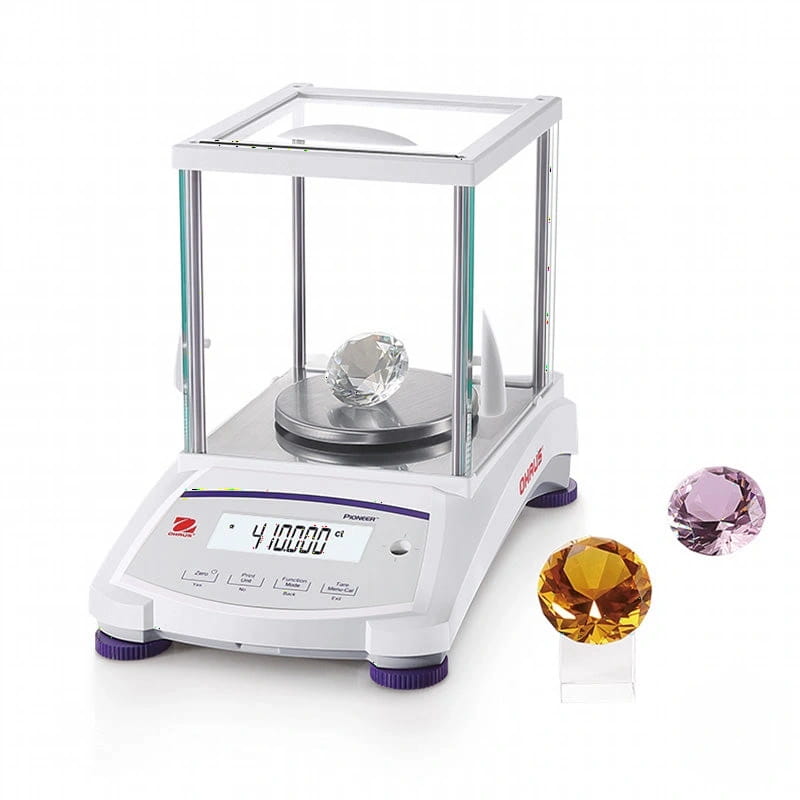 White pioneer ohaus analytical balance with a transparent glass enclosure and purple feet, displaying a clear faceted diamond on its weighing platform