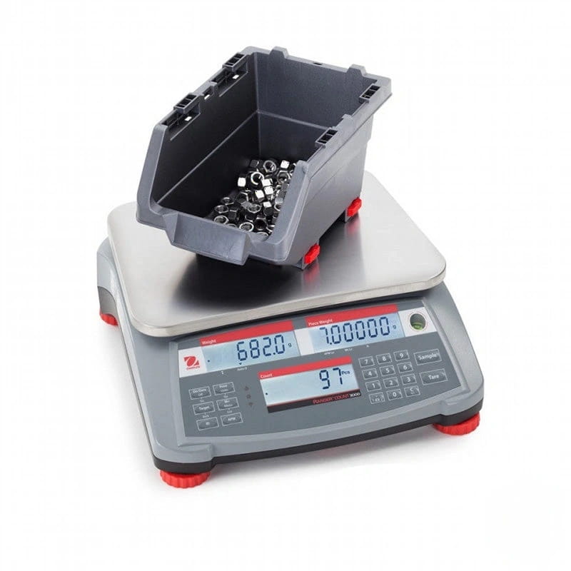 Gray digital scale with red feet and a gray plastic container filled with metal fasteners resting on its platform
