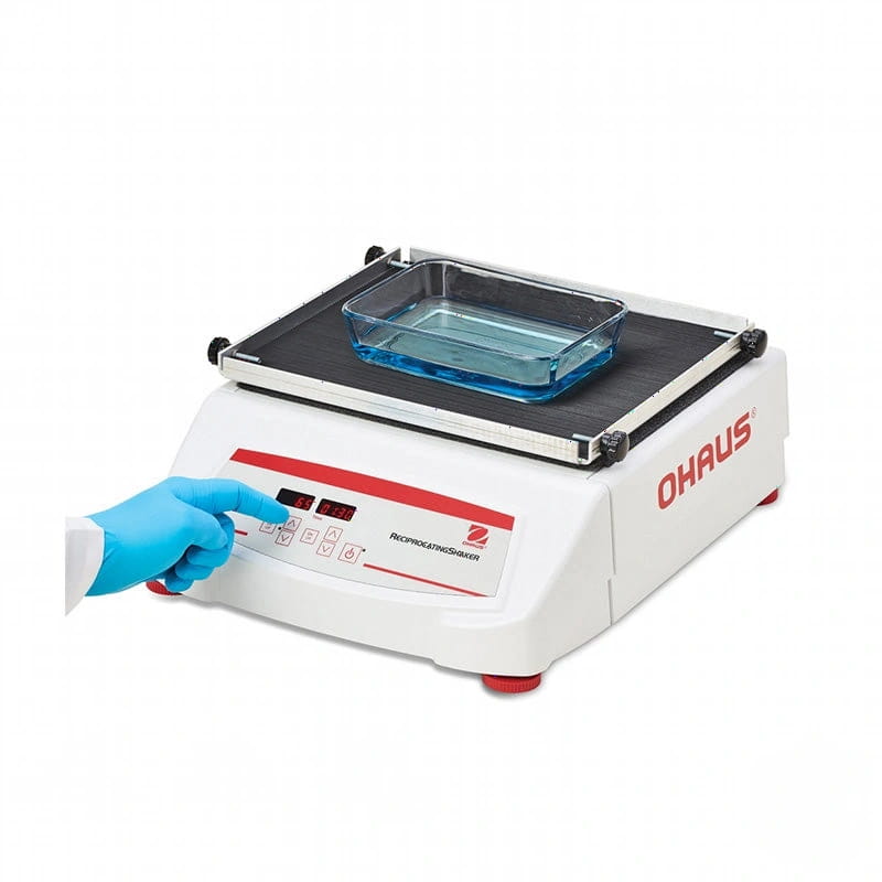 White ohaus reciprocating shaker with red accents and a digital control panel, featuring a clear glass container on its black platform