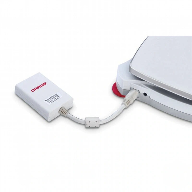 White ohaus digital scale adapter with a short cable connecting to the scale’s port