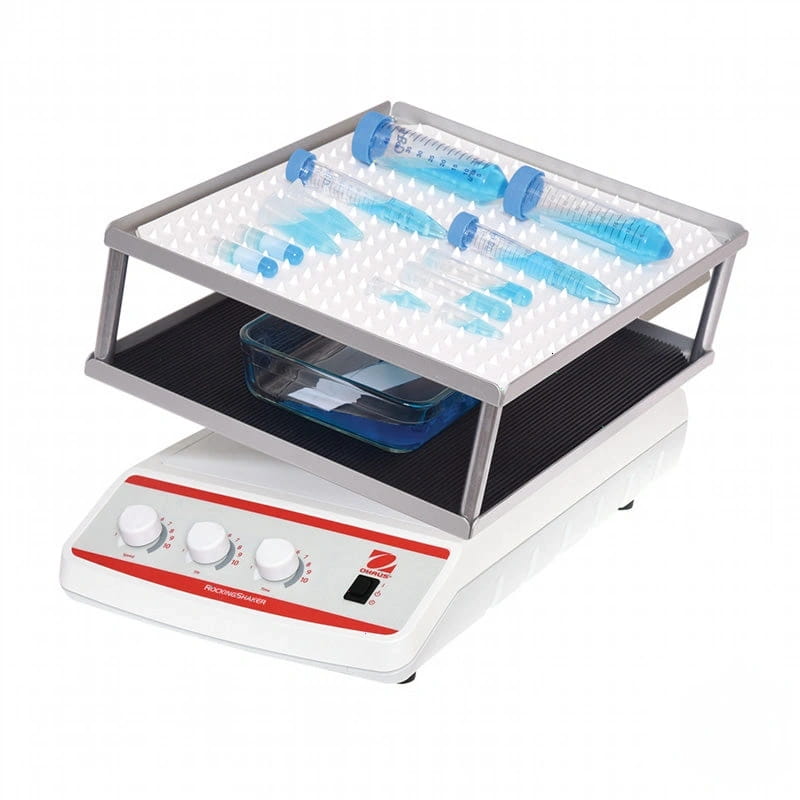 White and red laboratory rocker shaker with silver metal frame holding blue-tipped test tubes on a perforated tray above a glass container