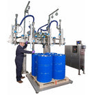 Industrial filling machine with stainless steel components and blue flexible hoses, positioned beside four bright blue plastic drums on a wooden pallet