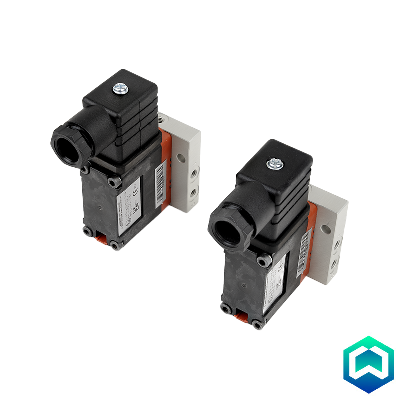 Two industrial solenoid valves with black bodies, white terminal blocks, and orange accent pieces, shown on a white background with a small blue and green logo in the bottom right corner. 